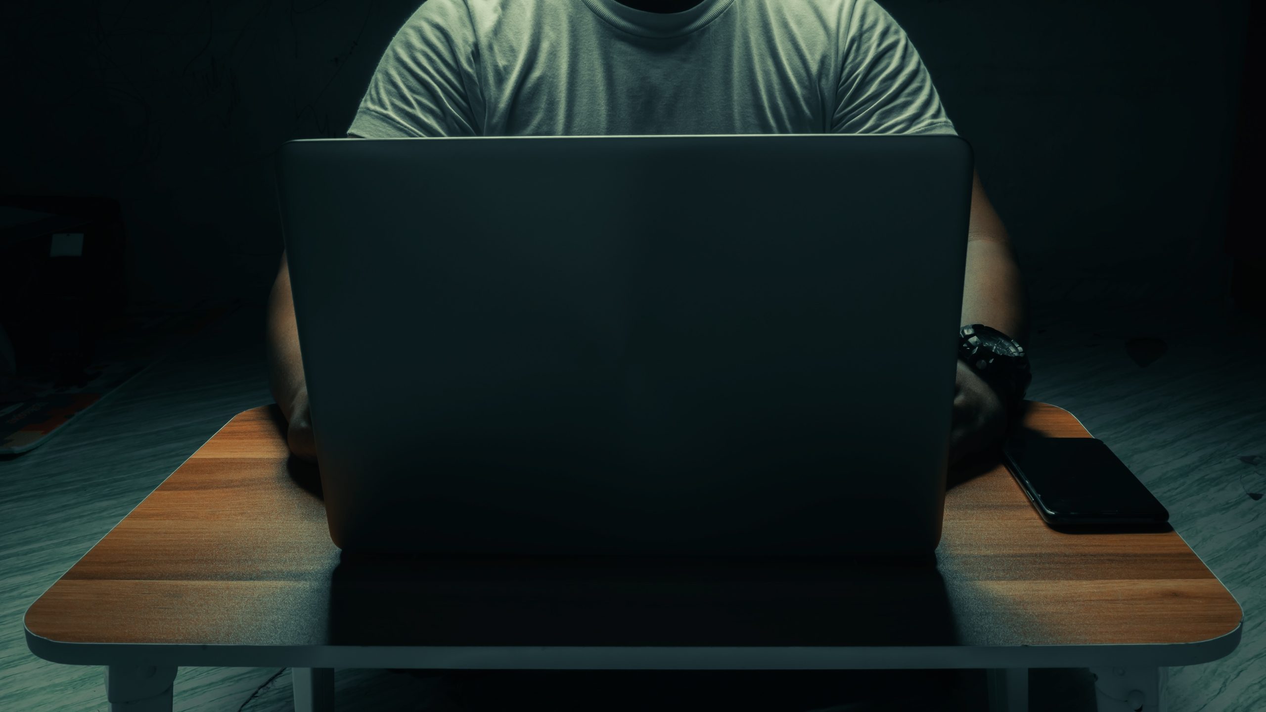 a man in a white shirt sits on a laptop in a dark room. with light shining down. internet concept addiction.topview.